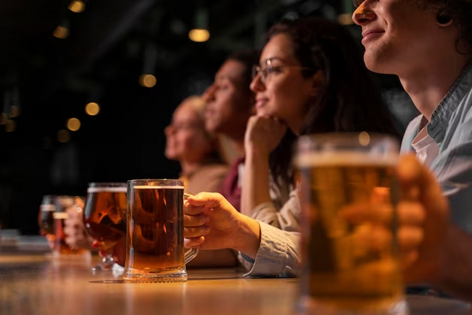 People at the bar, sitting in a row, each holding a glass of beer.